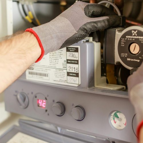 pexels-photo-7859953-7859953 Close-up of hands adjusting a boiler system with precise instrumentation, showing maintenance work.